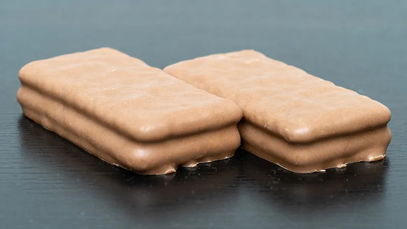 Close-up of two Tim Tam Original biscuits side by side on a dark table, showing the textured milk chocolate coating and layered sides