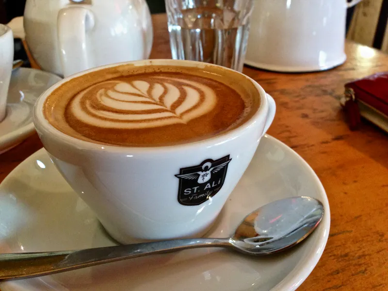 A Magic coffee with rosetta latte art in a small white St Ali cup and saucer on a wooden table